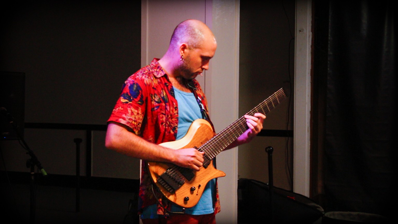 Ben Meyer performing on an eight-string guitar under stage lighting